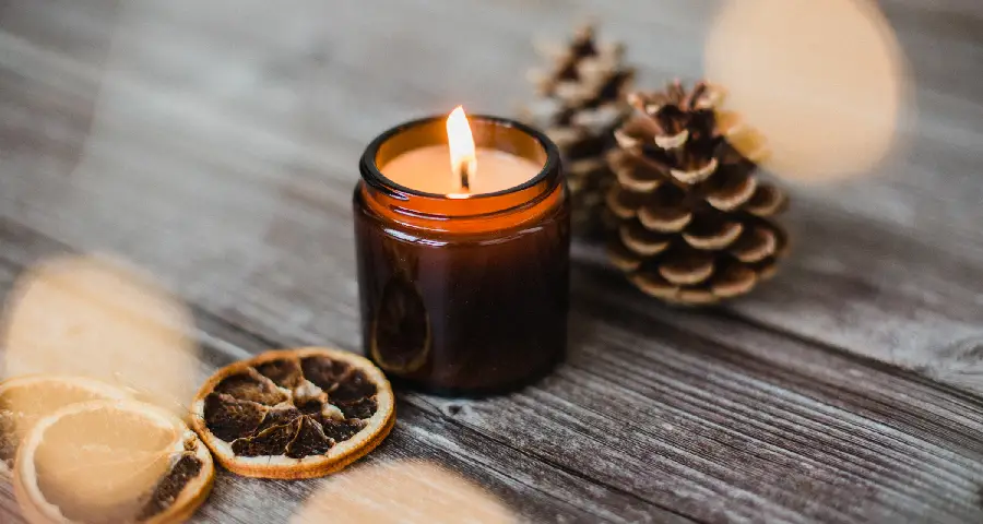 Mahogany teakwood candle burning in an amber jar with rustic wooden background